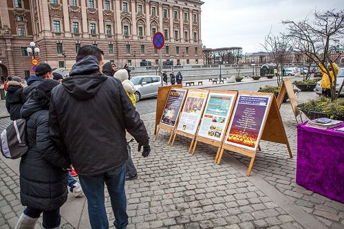 '图2，在斯德哥尔摩最热闹的皇宫旁的钱币广场上，民众观看展板，了解法轮功真相。'