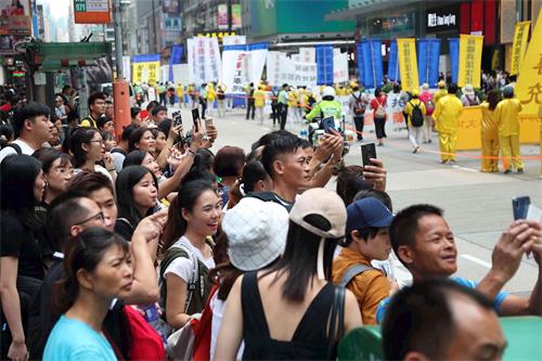 '图16：游行吸引沿路民众，许多人拿起手机拍摄盛况。'