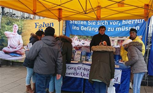 '图1～2：二零一九年十二月七日，法轮功学员在德国汉堡瑞生丹桥设立真相点，民众雨中签名，支持反迫害。'
