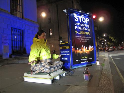 '图1： 二零一九年四月二十五日夜，法轮功学员高女士在伦敦中使馆前平抗议，法轮功学员在这里的持续和平抗议始于二零零二年六月。'