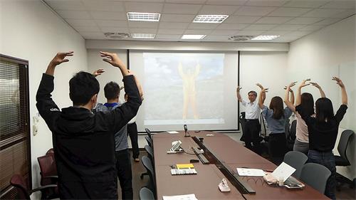 '图1：在公司会议室里举办的法轮功九天学法班，新学员们跟着教功录像带炼功。'