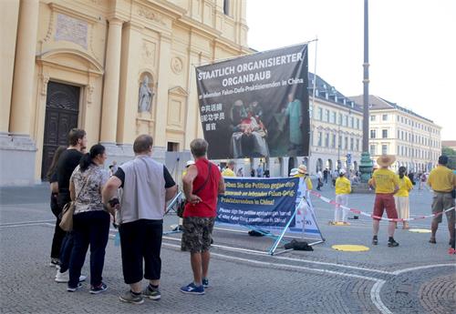'图1：二零二零年八月八日，法轮功学员在德国慕尼黑的奥迪安广场（Odeonsplatz）举办信息日活动。图为揭露中共活摘法轮功学员器官的大型图画。'