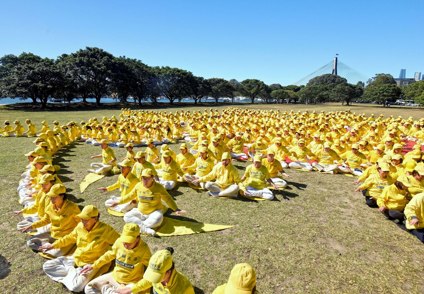 '图1~2:二零二五年十月十一日,在悉尼市中心银禧水滨公园,来自澳洲各地和新西兰的各族裔法轮功学员举行了排法轮图形和集体炼功的活动。排出的图形是巨大金色法轮,殊胜庄严。'